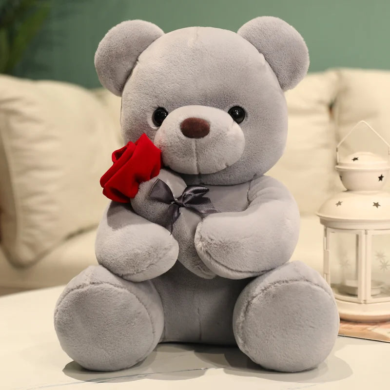 Gray teddy bear holding a red rose on a light-colored surface with a blurred background